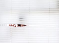 a woman peeking out from behind blinds with her hand on the window sill,