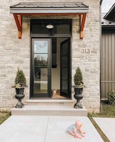 a baby laying on the ground in front of a house with two large planters