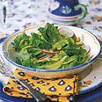 a salad in a bowl sitting on top of a blue and white plate with utensils