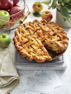 an apple pie with one slice cut out on a table next to apples and papers