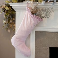 a pink christmas stocking hanging from a fireplace mantel with greenery and foliage