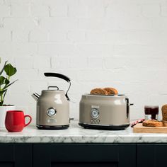 two toasters sitting on top of a counter next to coffee mugs and bread