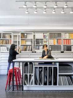 two people sitting at a table in front of bookshelves with lots of folders