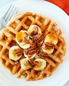 a white plate topped with waffles covered in bananas and pecans next to a fork