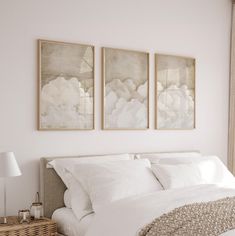 a bed with white linens and two paintings on the wall