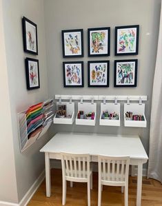 a white table and chairs in a room with pictures on the wall above it, along with small storage bins for children's artwork