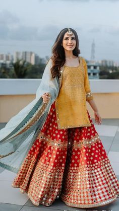 a woman in a yellow and red lehenga standing on top of a roof