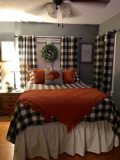 a bed with orange and black plaid covers in a bedroom next to a window covered by curtains