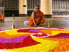 a man kneeling down in front of a flower arrangement on the ground with candles around it