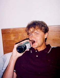 a man laying in bed drinking from a bottle with his mouth open and tongue out