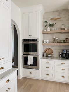 a kitchen with white cabinets and stainless steel ovens in the center, surrounded by wood flooring