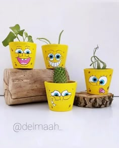 four yellow planters with faces painted on them sitting next to a wooden log and cactus