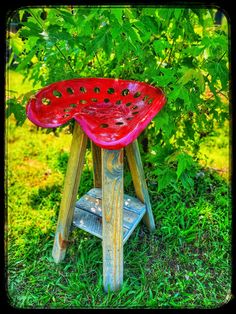 a red stool sitting in the grass next to a bush