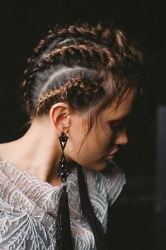 a woman with braids in her hair is wearing a white top and black earrings