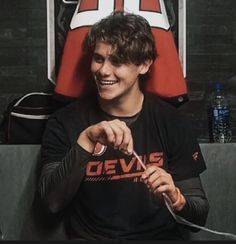 a smiling young man sitting in front of a red chair holding a knife and fork