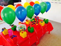 there are many balloons and gifts on the table at this birthday party with red cloth