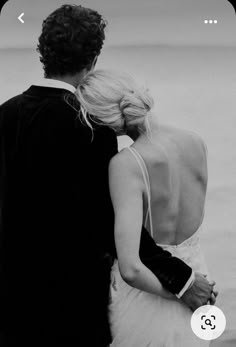 a man and woman standing next to each other near the ocean on their wedding day