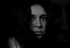 black and white photograph of a woman with long hair looking at the camera in dark room