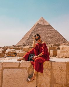 a woman sitting on top of a stone wall next to a large pyramid in the desert