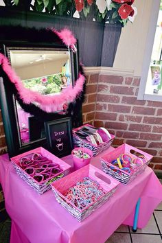 a pink table topped with lots of items next to a mirror and vase filled with flowers