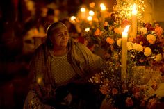 an old woman sitting in front of a table with flowers and candles on it at night