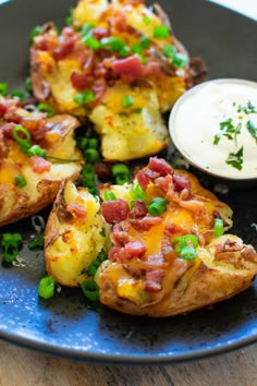 baked potatoes with bacon and green onions on a blue plate next to a small bowl of ranch dressing