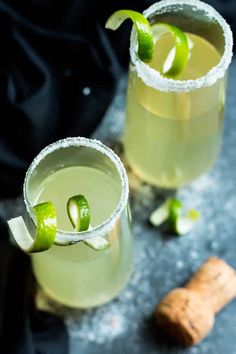 two glasses filled with drinks and garnished with limes next to a cork