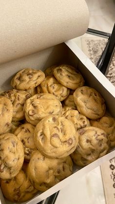 a box filled with chocolate chip cookies sitting on top of a table next to a roll of paper