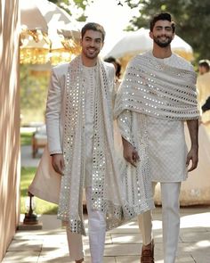 two men dressed in white are walking down the street with one wearing a shawl