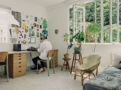 a woman sitting at a desk in front of a window with plants on the wall