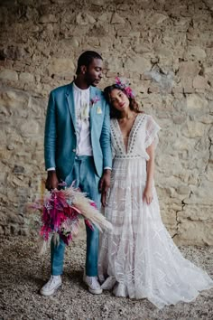 a man and woman standing next to each other in front of a stone wall