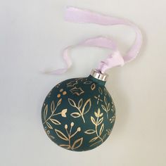 a green ornament with gold leaves on it hanging from a pink ribbon and white background