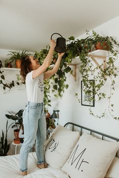 a woman is hanging plants on the wall above her bed while holding onto a hat