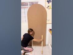 a woman sitting on a stool in front of a wall with an oval shaped door