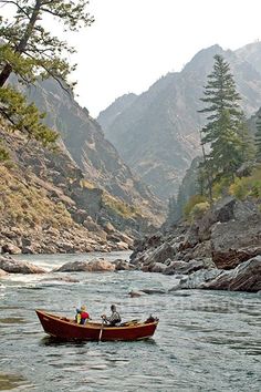 two people in a small boat on a river with mountains in the backgroud