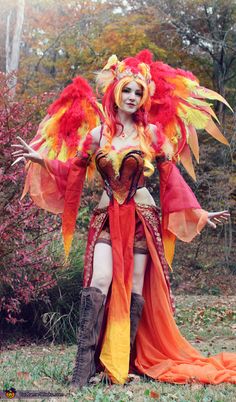 a woman dressed as a fairy with red and yellow feathers on her head, standing in the grass