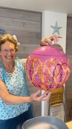 an older woman holding up a pink heart shaped object in front of a frying pan