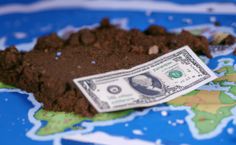 a pile of dirt sitting on top of a blue and white map with a one hundred dollar bill sticking out of it