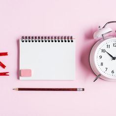 an alarm clock next to a notepad, pencil and eraser on a pink background