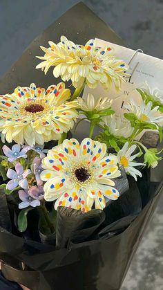 a bouquet of daisies and other flowers in a black paper bag with a book