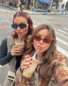 two women standing next to each other holding drinks in their hands and drinking from plastic cups