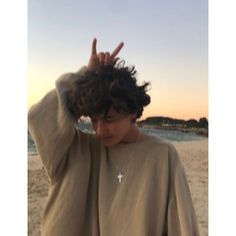 a young man standing on top of a beach holding his hands up in the air