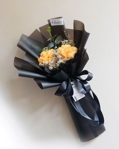 a bouquet of flowers is wrapped in black paper and tied with a ribbon on the wall