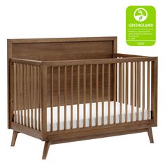 a wooden crib with white bedding and greenguard stickers on the side