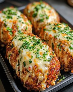 four meatballs covered in cheese and parsley on a baking tray with green garnishes