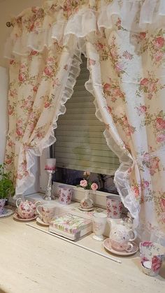 a window covered in pink flowers next to a table with cups and saucers on it