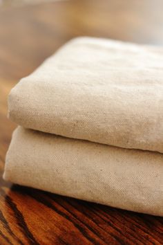 two pieces of linen folded on top of each other, sitting on a wooden table