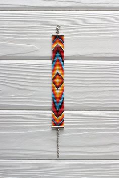 an orange and blue beaded bracelet hanging from a hook on a white wooden wall