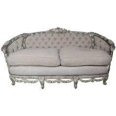 an antique style couch with white fabric and silver trimmings on the arms, sitting against