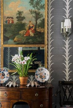 a table with plates and vases on it in front of a wallpapered painting